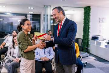 Front view of businesswoman receiving award from businessman in front of business professionals...