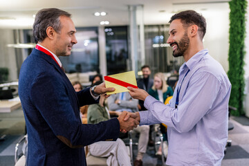 Front view of businessman receiving award from businessman in front of business professionals...