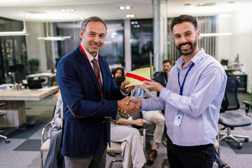 Front view of businessman receiving award from businessman in front of business professionals applauding at business seminar in office building