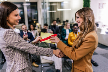 Front view of businesswoman receiving award from businesswoman in front of business professionals...