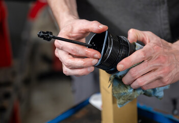 Close-up of hands cleaning a black car oil filter using a cloth in a garage. Maintenance concept