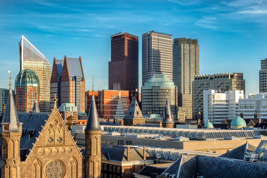 The Hague's historic and modern architecture merge into a vibrant cityscape featuring diverse skyscrapers and rooftops. A blue sky enhances the contrast between the ancient buildings and skyscrapers.