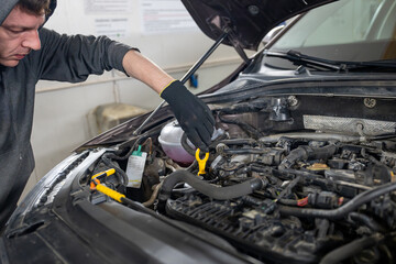 Mechanic wearing gloves inspecting a car's engine using a dipstick in a garage. Concept of vehicle maintenance and repair