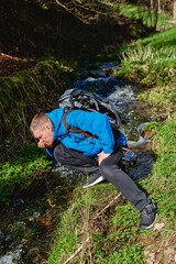 Hiker drinking stream water in mountain. Adult man drinking water from the mountain creek. Tourist...