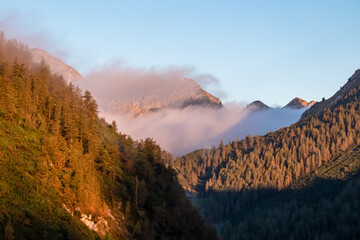 Cloud covered mountain peak Hochstuhl bathed in warm sunrise light seen from Loibl Pass in...