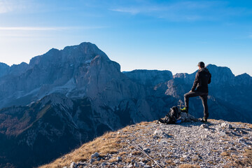Hiker man on mountain top of mount Piper overlooking majestic massif Jof di Montasion in Julian...