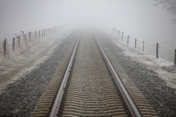 Fog-shrouded railway tracks stretch into a hazy distance.  Frost coats the ground.