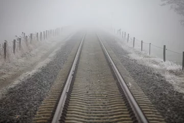 Fog-shrouded railway tracks stretch into a hazy distance.  Frost coats the ground.