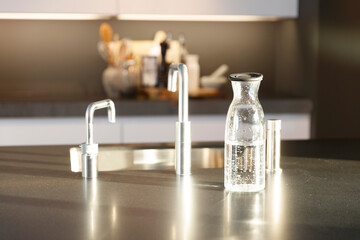 Glass water carafe sits on a stainless steel countertop.  Modern kitchen setting.