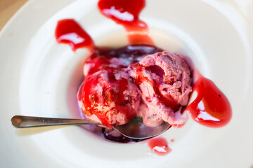 Closeup of ice cream with succades and fruit syrup on white plate with spoon..