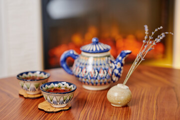 Hand-painted ceramic teapot with coordinating cups set on a warm wooden table. The delicate lavender sprigs and soft ambient light enhance the inviting and cozy tea ritual mood