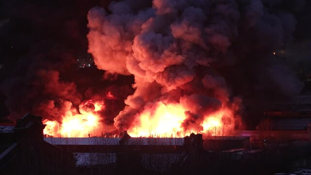 Orange toxic smoke from flames or fires of warehouses and industrial building at night. Burning house or adjacent area requiring the arrival of fire and rescue personnel due to fire safety violations.