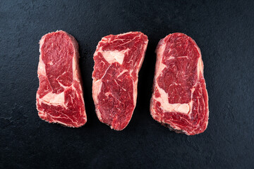 Dry aged raw beef entrecote cuts with fat marbling offered as top view on a black design board © HLPhoto