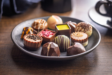 Mix of chocolate pralines on plate on wooden table.