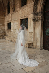 Naklejka premium beautiful bride dressed in a white dress stands in the middle of the old town. wedding photoshoot in the old town of Croatia. old medieval castle