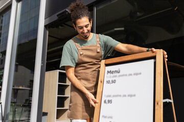 Cafe worker setting up menu board outside trendy coffee shop