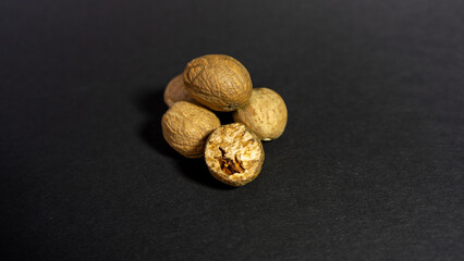 Nutmeg lies on a black background, with one partially grated. Close up.

