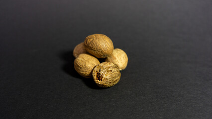 Nutmeg lies on a black background, with one partially grated. Close up.

