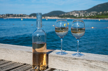 Tasting of cold rose wine from Provence outdoor on wooden yacht pier with view on blue water and white sandy beach Plage de Pampelonne near Saint-Tropez, summer vacation in France