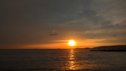 A boat floating on the calm ocean as the sun sets in the background.