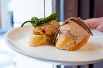 Typical snacks of Basque Country, pinchos or pinxtos skewers with small pieces of bread, fish, sea food, sweet green pepper served in bar in San-Sebastian or Bilbao, Spain
