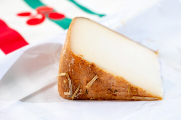 Piece of tasty Basque Brebis Fume smoked sheep cheese produced in south-western France, Northern Basque Country and towel with Basque symbol and colours