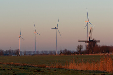 Wind turbines and a traditional windmill stand in a field at dawn or dusk.  Rural Dutch landscape.