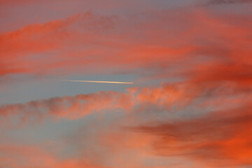 Sunset sky, streaked with clouds and an airplane contrail.  Warm colors, soft light.