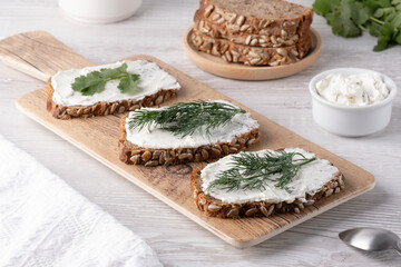 Freshly prepared whole grain bread slices topped with creamy spread and garnished with cilantro on a wooden cutting board.