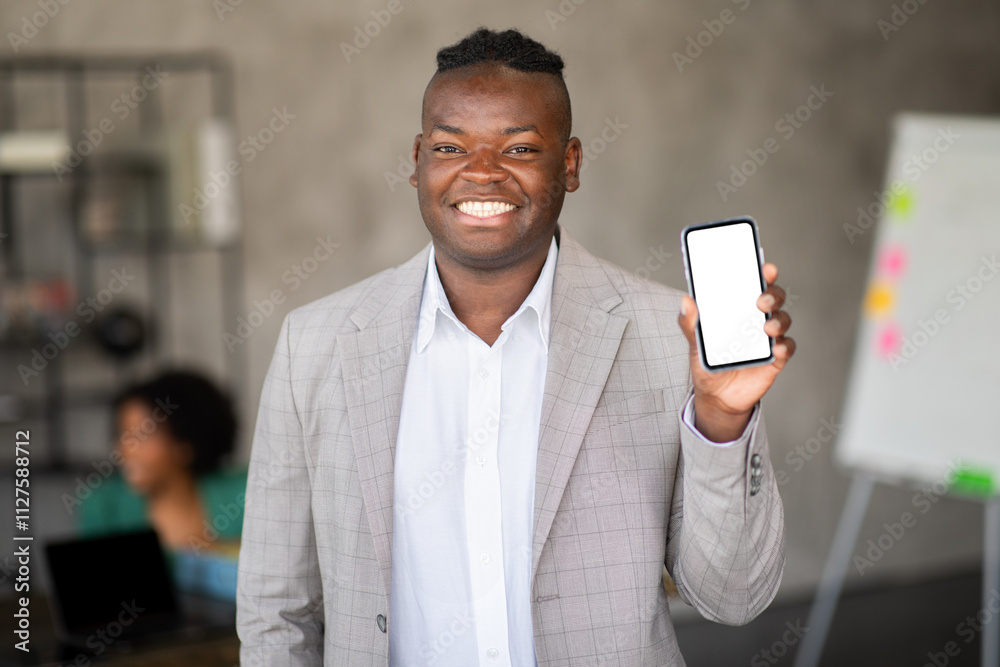Aufkleber A smiling man in a suit holds up his smartphone while others work in a diverse office. The setting reflects collaboration and a focus on teamwork within a corporate atmosphere.