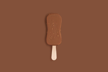 Chocolate ice cream on a stick with nuts and chocolate glaze on a brown background. Monochrome minimal food photo concept, top view