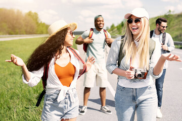 Group of multinational millennial friends walking along highway, chatting to each other, laughing,...