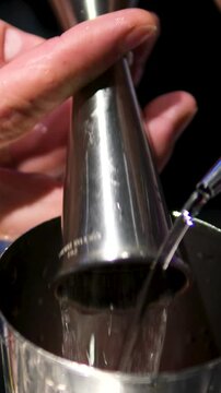 Young bartender pours drink into glass on counter in trendy bar.