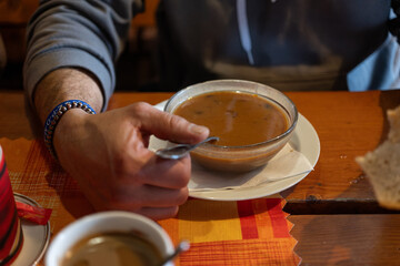 Glass bowl with goulash soup and a man's hand.

