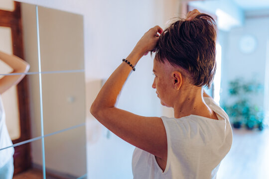 A woman with cancer sitting comfortably on the couch adjusts her short wig, an image of self-care, relaxation, and a moment of reflection in her personal space.