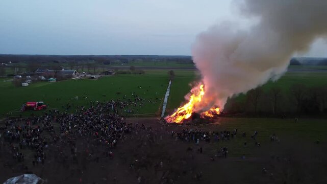Elsloo, the Netherlands - April 9th 2023: Rotating drone footage of people gathering around the annual Easter bonfire.