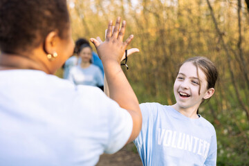 Motivated cheerful child sharing high five with her friends, finishing litter cleanup of the woodland and saving the ecosystem. Satisfied volunteers congratulating and praising each other.