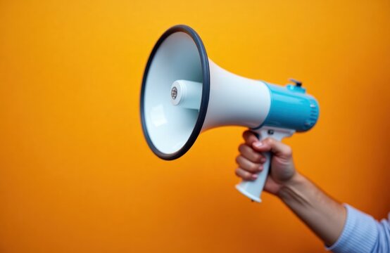 Person holds megaphone against bright orange background. Hand holds loudspeaker. Scene suggests announcement communication. Image suitable for themes like protests, news, announcements, public - Powered by Adobe