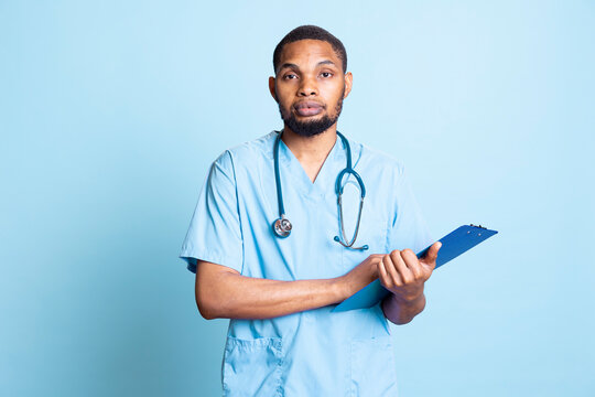 African american medical staff having the test results on clipboard papers, using the patient records to provide with the right diagnosis. Male nurse with scrubs and stethoscope offer services.