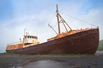 Abandoned rusty ship Garðar on an Icelandic shore in the Westfjords, under a blue sky.