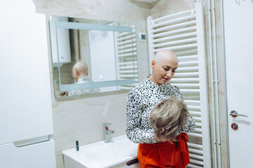 A bald woman suffering from cancer tenderly holds a wig in front of the mirror, embodying courage...