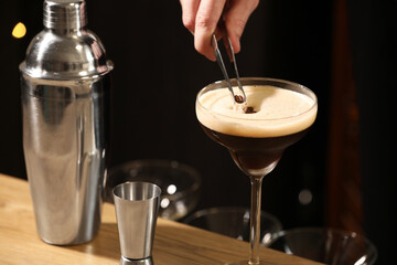 Bartender putting coffee bean into glass with delicious espresso martini at wooden table in bar,...