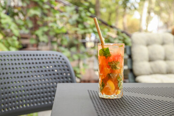 Glass of tasty refreshing drink and straw on table in outdoor cafe