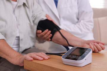 Doctor measuring patient's blood pressure at wooden table indoors, closeup