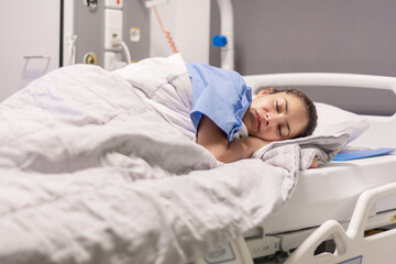 Young female patient of the clinic in blue robe sleeping on hospital bed in calm environment in private room, soft lighting, concept of recovery and care, copy space