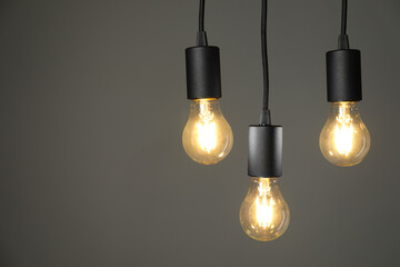 Light bulbs hanging on cords against grey background, space for text