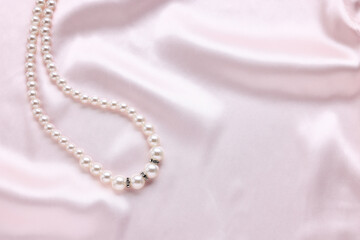 Elegant pearl necklace on pink fabric, top view. Space for text