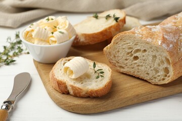 Cut baguette with butter and herbs on white wooden table, closeup