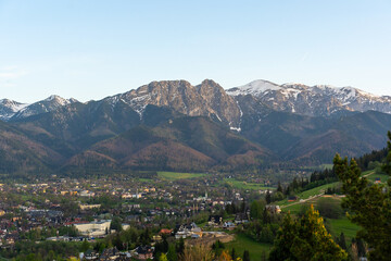 Fototapeta premium Scenic mountain view of Tatra peaks and Zakopane town during springtime at sunset, featuring lush greenery and picturesque buildings. Concept of nature, tranquility, and Polish landscapes.