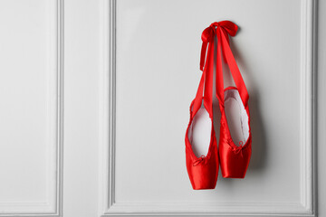 Pair of beautiful red pointe shoes hanging on white wall, space for text © New Africa